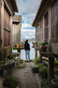 Man standing between traditional Combarro horreos, looking out over the calm sea and horizon, enjoying the scenic coastal view from the historic fishing village
