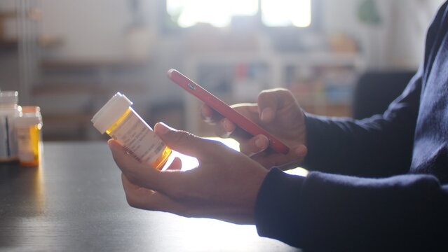Person using smartphone for healthcare management, scanning prescription medicine bottle for refill or information, managing personal medication digitally