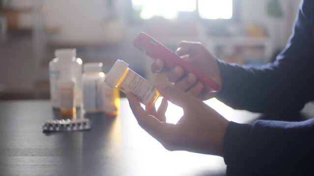 Person using a smartphone to scan a prescription medication bottle, managing health information and prescriptions digitally, accessing pharmacy services online for medical treatment