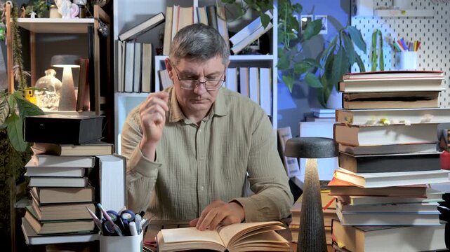 Tired man studying with book on head surrounded by stacks of literature, Overworked student feeling pressure during late study session