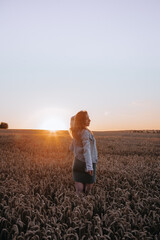 Fototapeta premium Pregnant woman holding baby socks in wheat field at sunset. 