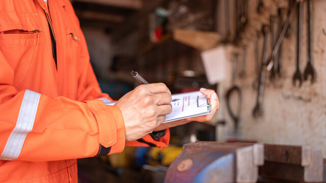 An engineer is checking on chemical hazardous material checklist form with background of storage warehouse at factory workplace. Industrial safety working scene, close-up and selective focus.