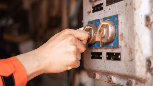 Action of an electrician hand is turning on lighting switch at electrical junction box, during inspection and maintenance job. Industrial working scene with the equipment, close-up.