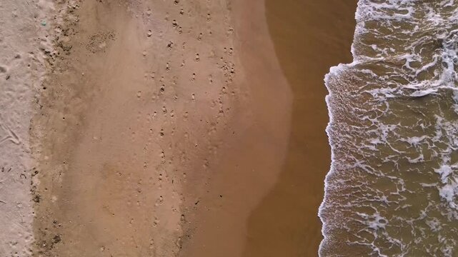 The video captures an aerial view of a sandy beach in La Guajira, Colombia, with clear wave patterns and footprints on the shore.