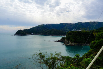 Coastal bay and forested mountains with sun rays over village on Shikoku Henro route Japan