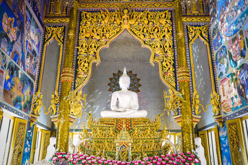 Majestic white Buddha statue with intricate golden altar and surrounding mural paintings in a beautiful Thai temple. © ball