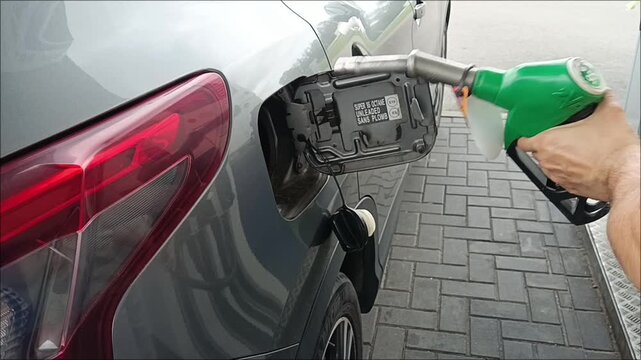 Close up of a man refilling his car at a gas station, a direct visualization of the global energy crisis, fuel price inflation, and economic burden.