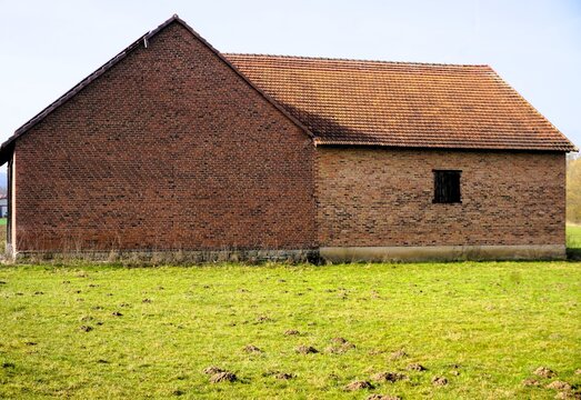 Alte rotbraune Backsteinscheune hinter gr&uuml;nem Ackerfeld bei Sonne am Morgen im Fr&uuml;hling