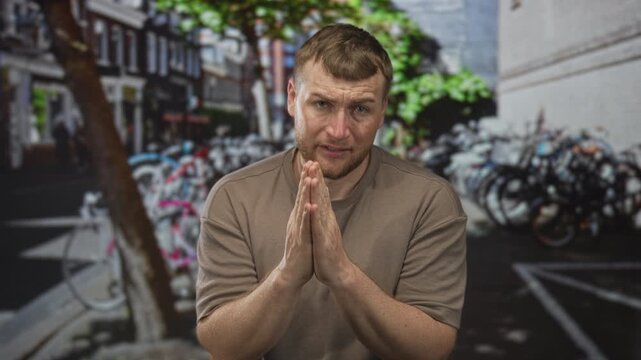Man with hands pressed together in prayer on a crowded amsterdam street, pleading for forgiveness; apology plea pleading.