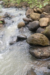 Obraz premium Turbid water flowing rapidly through a rocky riverbed surrounded by natural vegetation.