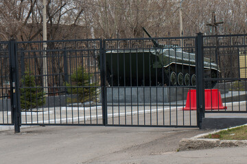 A green tank on a pedestal behind a fence.