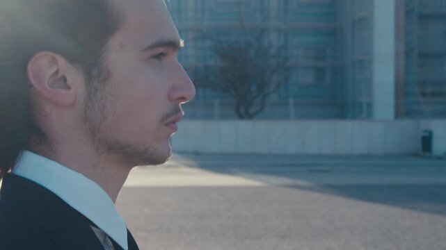 Profile view, close-up of the face of a young man in a stylish classic business suit with a tie, who walks alone in a deserted city. Slow motion.