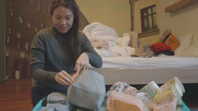 A focused individual sorts through personal items in a cozy bedroom, creating a tidy, organized space. The scene highlights the importance of decluttering for a peaceful environment.