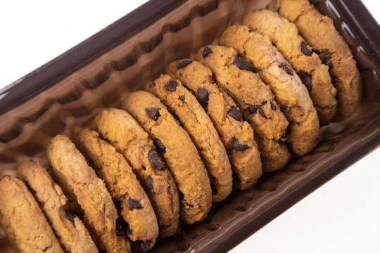 Row of fresh chocolate chip cookies packaged in a brown plastic tray, isolated on a white background.