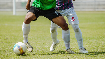 Naklejka premium Football players in action chasing the ball across a green soccer field, showing fast movement, athletic strength, competitive sports atmosphere, teamwork, outdoor activity, and intense game moment
