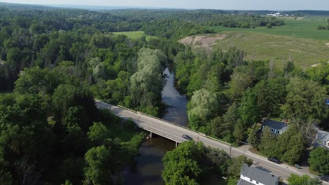 Flying north over the Creditview Road bridge over the Credit River in the Cheltenham area, a community within the town of Caledon, Ontario, Canada. Shot by a drone on a hazy summer afternoon.