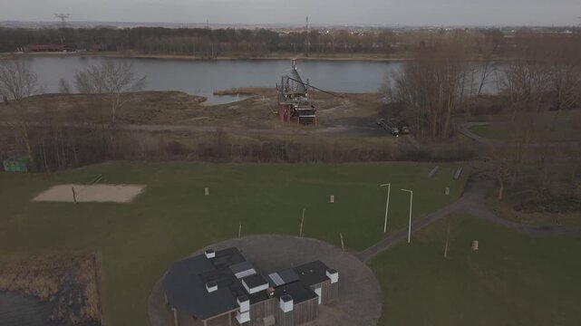 Drone flyby shot of abandoned mining tower over water with busy roads 