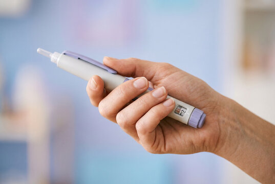 Hand holding insulin pen injector on soft blurred background, medical device for self injection and chronic disease management.