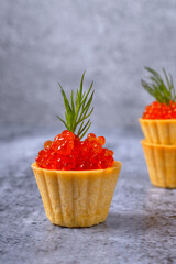 Red caviar tartlet decorated with dill appetizer against the gray background. Close-up
