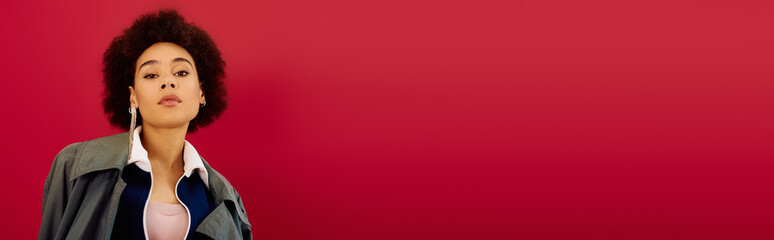 Stylish woman with curly hair showcasing modern fashion against a vibrant red backdrop