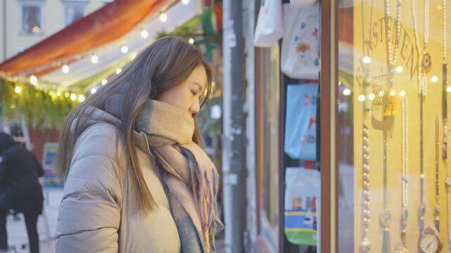 A serene scene of a woman admiring window displays in a charming winter market, surrounded by colorful decorations and lights. The festive atmosphere captures the joy of shopping during the holiday se