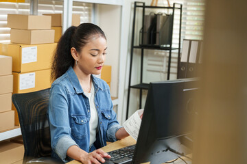 Asian adult woman startup entrepreneur managing e-commerce orders, typing inventory updates on...