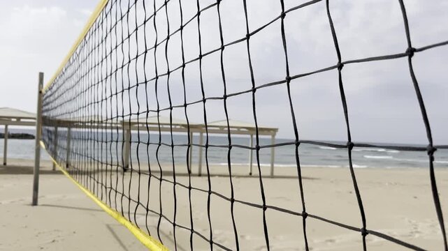 Camera moves along a volleyball net on the beach of Haifa, Mediterranean Sea, capturing the sand, sea, and shoreline atmosphere.