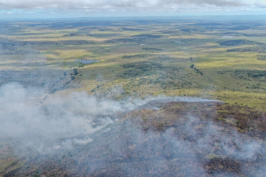 Aerial view of a landscape scarred by a recent fire with smoke drifting across the terrain, Welgevonden Game Reserve, Limpopo, South Africa.