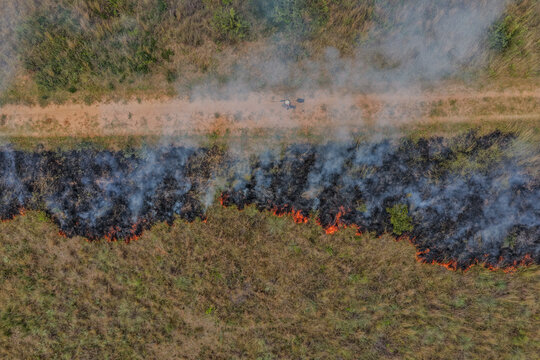 Aerial view of controlled burn sweeping through Welgevonden Game Reserve, painting the landscape with fiery hues against the golden veld, Vaalwater, South Africa.
