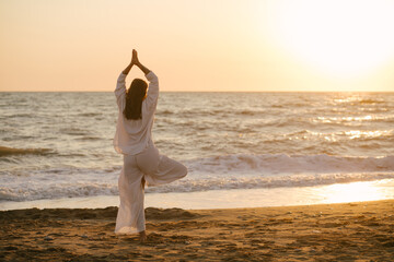 Beautiful 40 years old woman having yoga exercises on th beach at sunset.