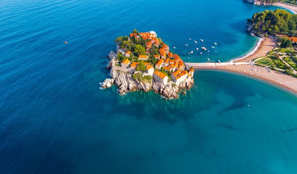 Aerial view of the island connected by a narrow isthmus, the terracotta roofs contrasting with the turquoise waters, Sveti Stefan, Budva Municipality, Montenegro.