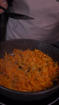When preparing the vegetable base for the soup, the cook mixes grated carrots and finely chopped onions in a saucepan.