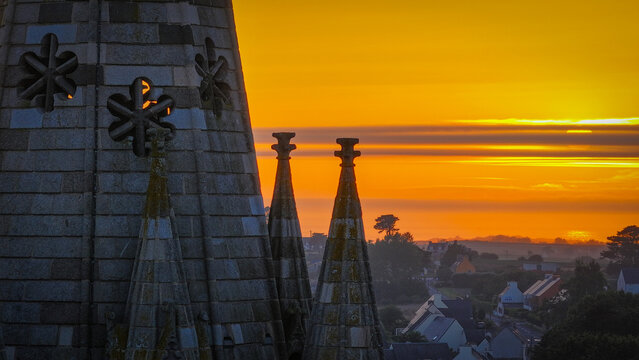 Aerial view of the cathedral spires reaching towards the golden sunrise horizon, casting long shadows over the town, Saint-Pol-de-Leon, Brittany, France.