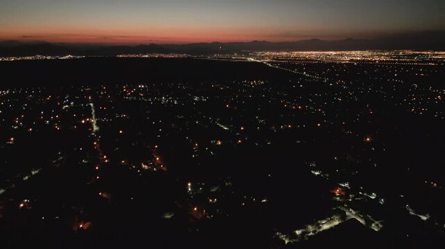 Aerial Drone View of City Lights Glowing at Dusk with mountains in the background