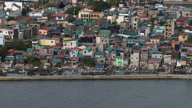Aerial view of densely packed buildings meet the sea, a mosaic of colors and textures under a bright sky, Navotas, Metro Manila, Philippines.