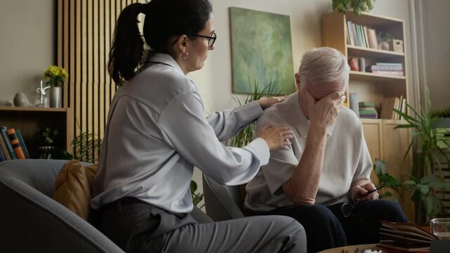 Handheld slowmo shot of empathetic middle-aged Caucasian female psychologist comforting depressed gray-haired man covering face with hand during individual therapy session in office