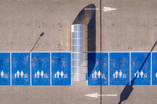 Aerial view of blue family parking spaces divided by a glass structure, the sunlight casting long shadows, Warsaw, Masovian Voivodeship, Poland.