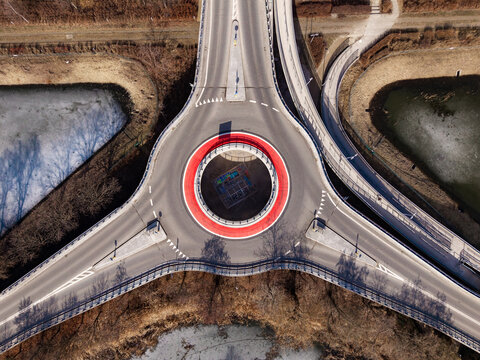 Aerial view of a roundabout with a striking red circle, connecting roads like veins on a leaf, framed by the stark beauty of winter's edge, Warsaw, Masovian Voivodeship, Poland.
