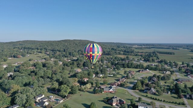 Aerial view of a vividly colored hot air balloon drifting serenely over a landscape of verdant trees and quaint houses, Huntsville, Alabama, United States.