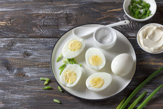 Boiled eggs with green onion, salt and mayonnaise on plate over wooden table