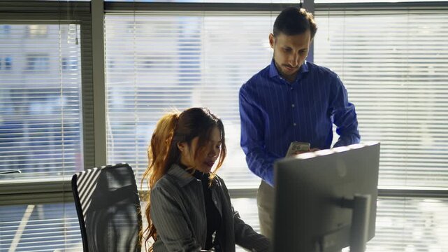Two business professionals engage in a collaborative discussion and document exchange in a bright office environment. They are focused on their work, showcasing effective teamwork and communication.
