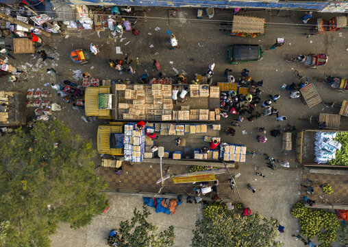 Aerial view of bustling market with yellow trucks loaded with goods amidst a vibrant scene of commerce and activity, Dhaka, Dhaka Division, Bangladesh.