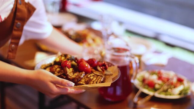 Female waiter in uniform serving dishes and drinks on outdoor party, server carrying plates with food and beverages at the table, catering service wedding reception, personnel in cafe, staff on event