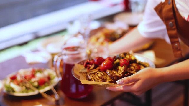 Female waiter in uniform serving dishes and drinks on outdoor party, server carrying plates with food and beverages at the table, catering service wedding reception, personnel in cafe, staff on event