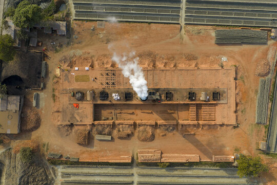 Aerial view of brick factory billowing smoke against the backdrop of orderly rows of bricks, creating a stark contrast between industry and production, Dhaka, Dhaka Division, Bangladesh.