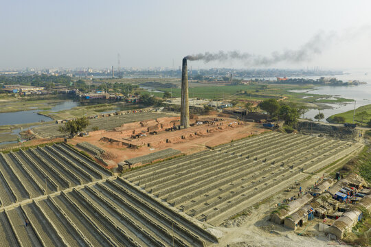 Aerial view of brick factory spewing smoke into the atmosphere contrasting with the adjacent river, Dhaka, Dhaka Division, Bangladesh.
