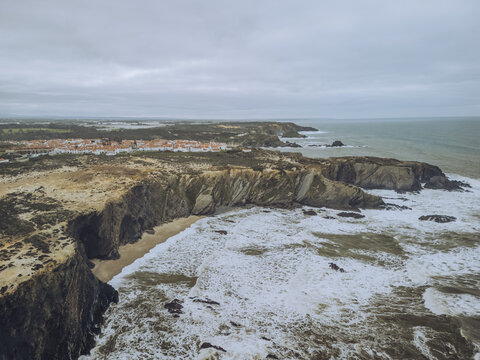 Aerial view of rugged cliffs meet the turbulent sea, showcasing the dramatic coastline near the town, Zambujeira do Mar, Beja District, Portugal.