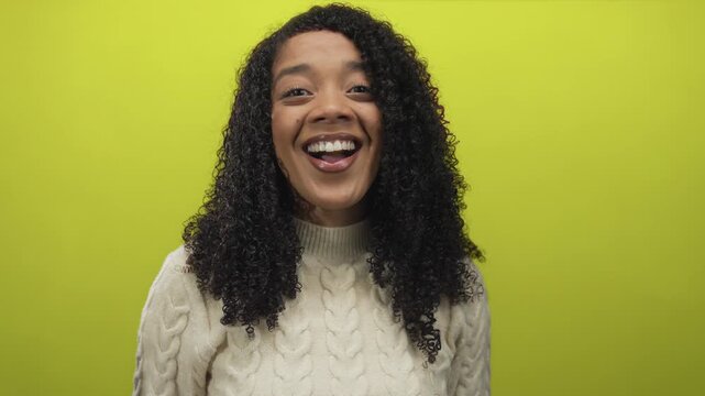 Woman wearing a cable knit sweater smiling and showing teeth in studio with lime green background; confidence.