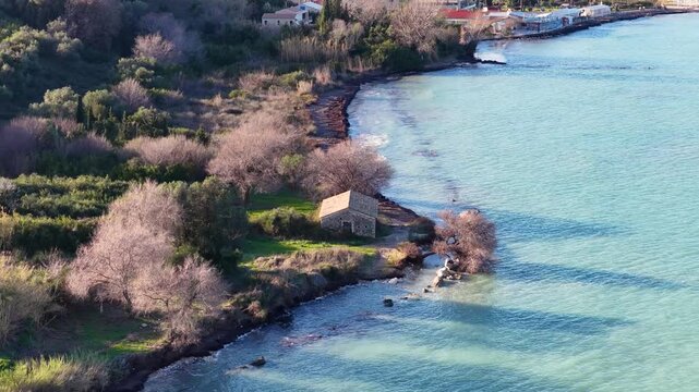 Scenic Aerial View of Old Stone House on the Coastline of Roda Corfu Surrounded by Trees and Turquoise Water