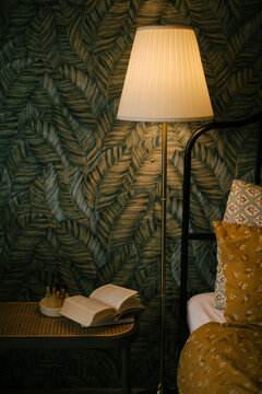 Cozy room with floor lamp and open book on the table near bed.
